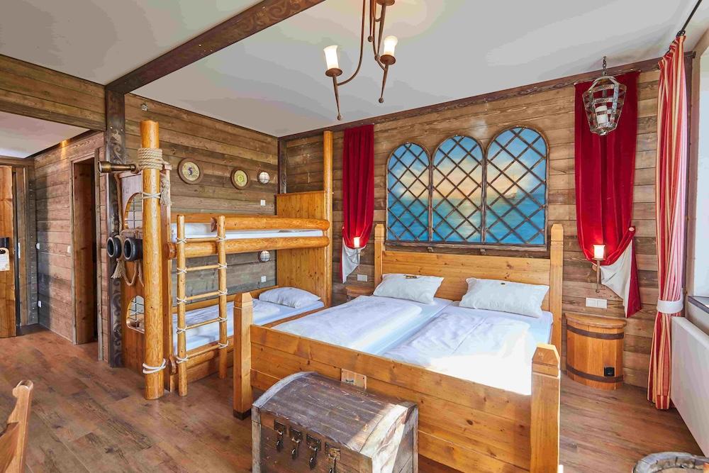 A wooden hotel room with a double bed and two bunk beds next to each other. The beds are made with white sheets and the room is tidy and ready for guests.