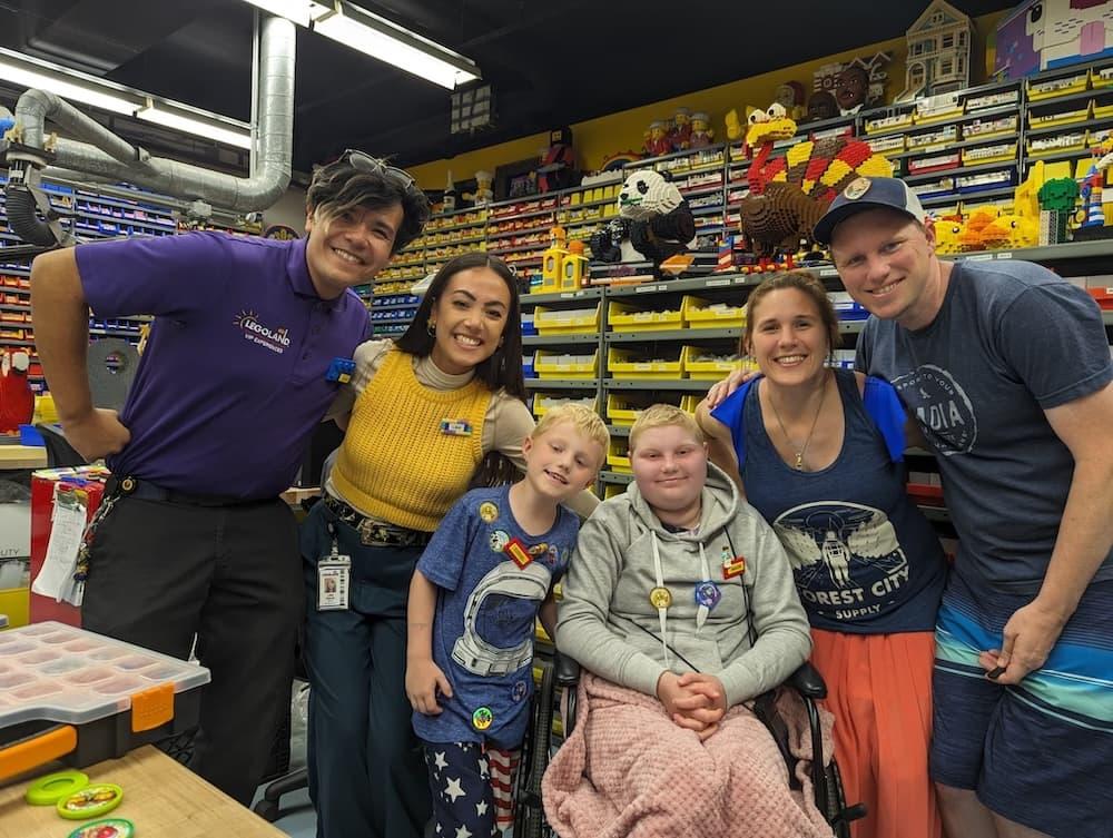 Two LEGOLAND workers smile alongside a young girl Maddie and her family as they visit LEGOLAND. The photo is inside the workshop.