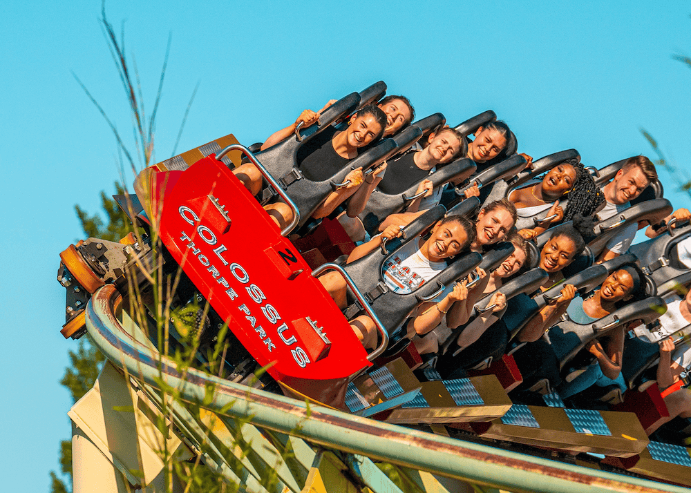 A rollercoaster with a red front in filled with people and moving along a yellow track