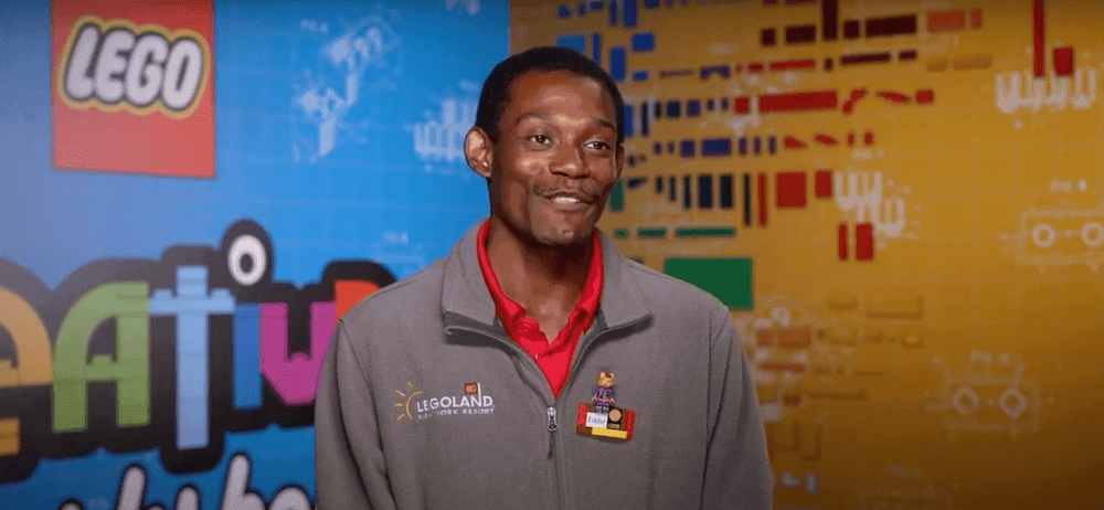 Man in a grey jumper and red polo shirt is standing infront of a LEGOLAND® background