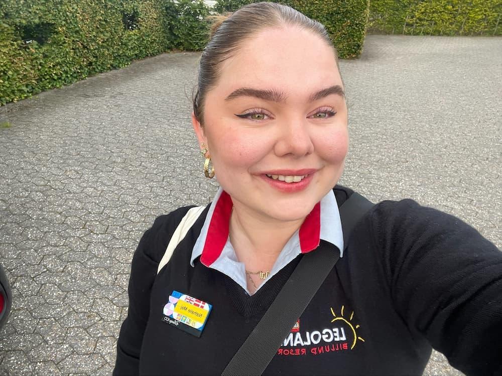 Selfie of a female LEGOLAND® employee in a navy blue uniform outdoors smiling.