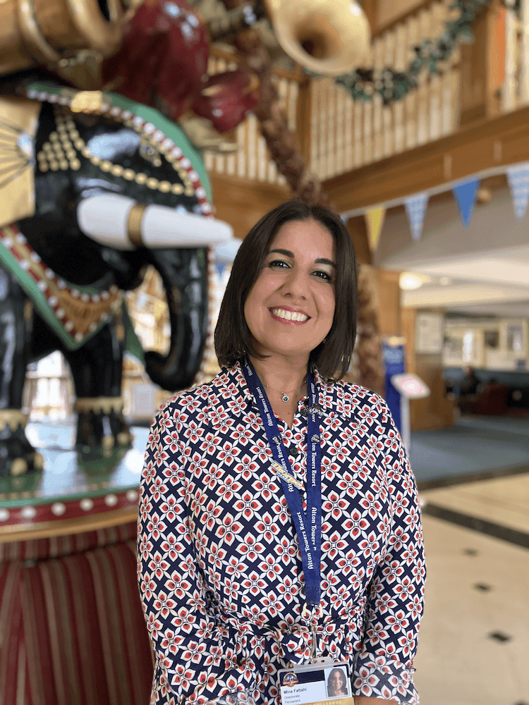 Women with black hair in an orange and blue patterned shirt and blue lanyard stood in front of an elephant ornament.