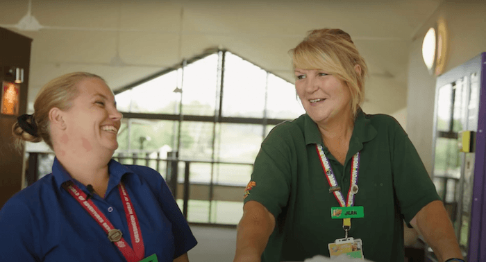 Two blonde women wearing Chessington lanyards smiling each other, one in a green polo and one in a blue polo.