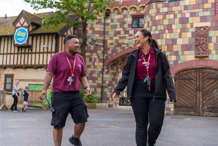 A male and a female in Burgundy Chessington World of Adventure polo shirts are walking together and smiling.