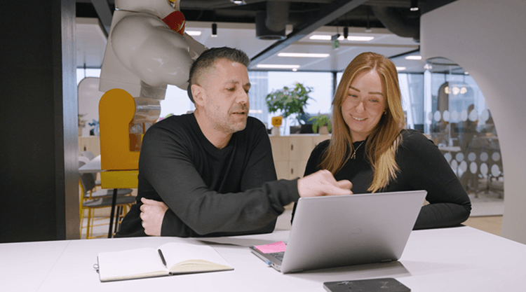 Two people sitting next to each other looking at a laptop. They are smiling and engaged in a conversation.